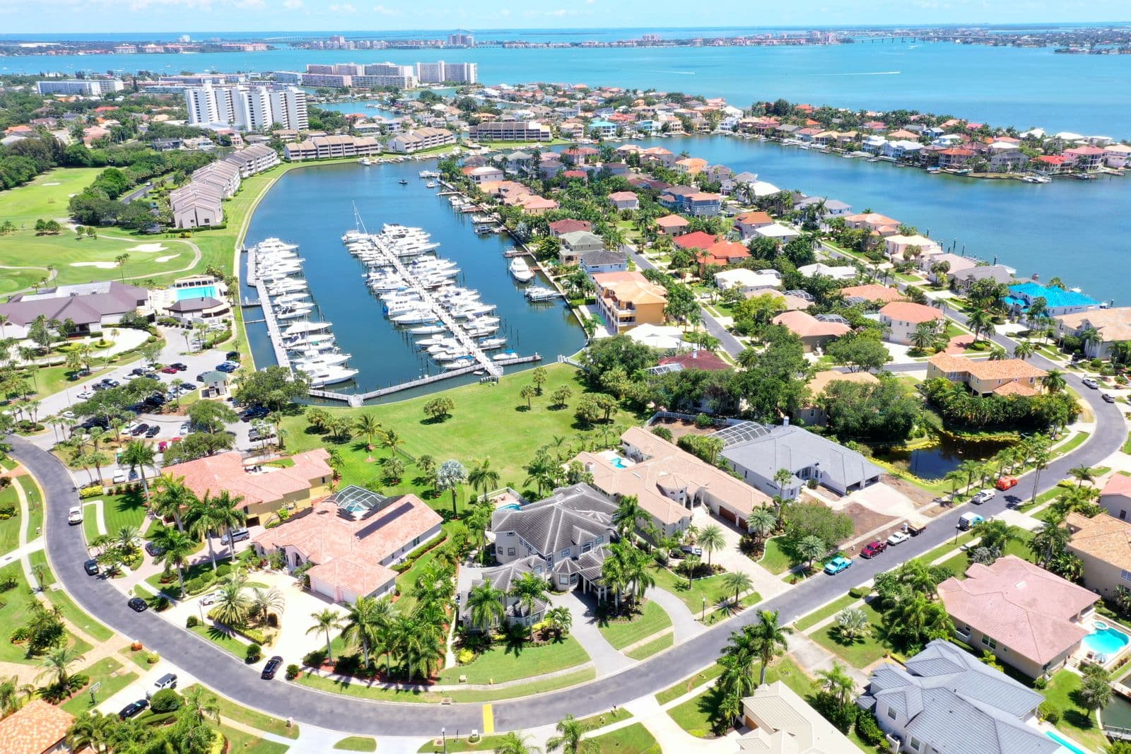 Aerial view of a coastal neighborhood featuring luxury homes, a marina, and sparkling blue water.